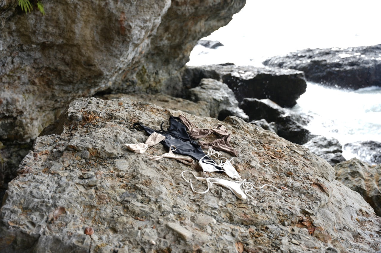 meelah swim born goddess bikini collection layed out on beach rocks shorefront